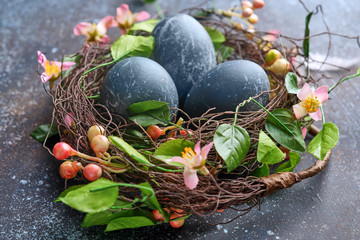 Blue easter egg in nest with flowers on dark vintage background