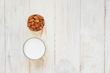 Homemade Almond milk in a bottle and nuts in white porcelain bowl on wooden background. Top view, copy space