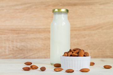 Homemade Almond milk in a bottle and nuts in white porcelain bowl on wooden background