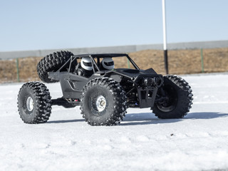 Fototapeta na wymiar Radio controlled car models: a small black buggy toy with dirty splashes stands in the snow.