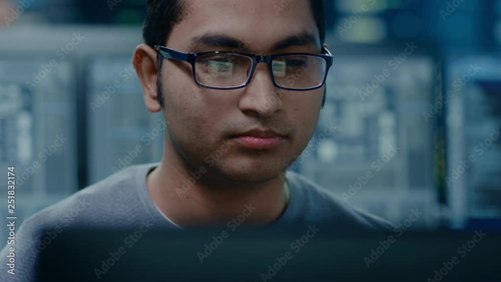 Poster Portrait of a Smart and Handsome IT Specialist Working on a Personal Computer. In the Background Bokeh Shot of Personal Computers with Screens in Technologically Advanced Data Research Center