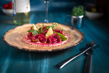Vegan red ravioli with beetroot on a plate in cream sauce, serving in a restaurant on a wooden...