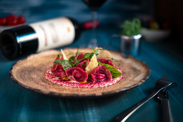 Vegan red ravioli with beetroot on a plate in cream sauce, serving in a restaurant on a wooden background