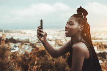An excited young African female with braids is smiling and photographing cityscape from the...