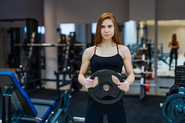 Young beautiful girl athlete bodybuilder does exercises in the modern gym. Concept - the power of beauty, fashion, diet, sports nutrition, sportswear.