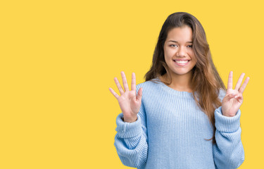 Young beautiful brunette woman wearing blue winter sweater over isolated background showing and pointing up with fingers number eight while smiling confident and happy.