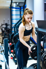 Fototapeta na wymiar Young beautiful fitness girl posing in gym with sports equipment