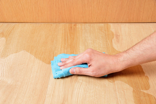 Man hand wiping wooden laminate parquet floor with blue sponge