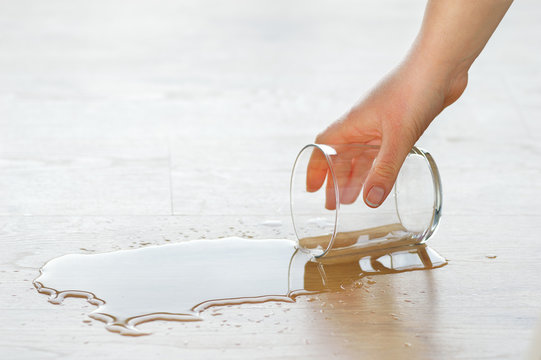 Close up of a hand holding a glass of water from a laminate wood floor
