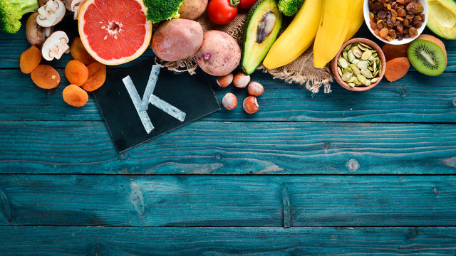 Foods containing natural potassium. K: Potatoes, mushrooms, banana, tomatoes, nuts, beans, broccoli, avocados. Top view. On a blue wooden background.