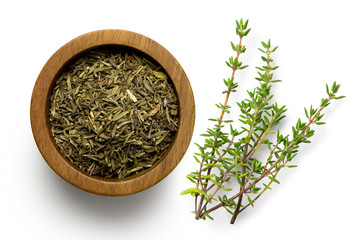 Dried rubbed thyme in a dark wood bowl next to fresh thyme sprig isolated on white from above. - obrazy, fototapety, plakaty
