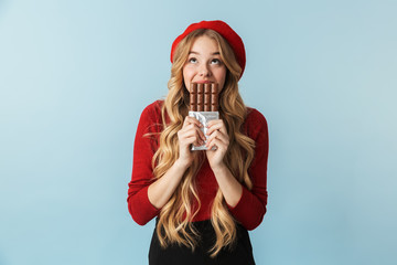 Image of blond girl 20s wearing red beret eating chocolate bar