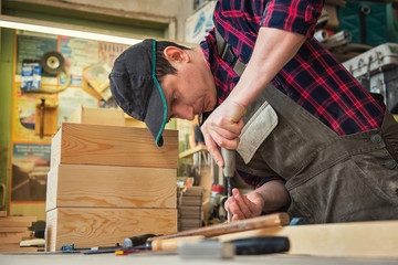 Carpenter working with a chisel and hammer in a wooden workshop. Profession, carpentry and manual woodwork concept.