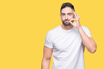 Handsome man wearing white t-shirt over yellow isolated background mouth and lips shut as zip with...