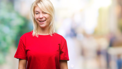 Young beautiful blonde woman wearing red t-shirt over isolated background winking looking at the...