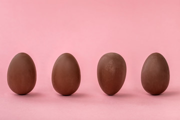 row of unstable chocolate eggs on pink background with copy space, funny creative concept