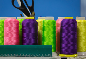 the thread of acid colors in coils with a ruler and scissors stand on a blue background