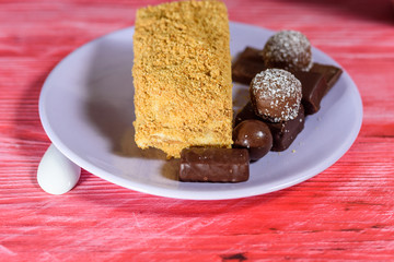 Layered sponge cake, chocolate sweets and cup of coffee on wooden background.