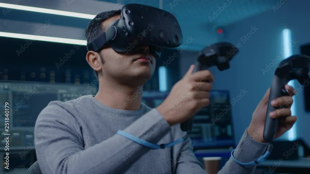 Aufkleber Software Delevoper Wearing Virtual Reality Headset Gesturing with Controllers to Develop and Program VR Gaming and Applications. In the Background Technology Developing Studio with Computers Monitors