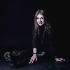 portrait of a young girl in a black dress on a dark background sitting in the studio