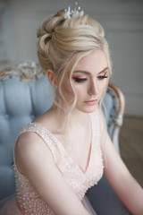 Gentle portrait of an elegant blonde bride in a light pink dress in the interior.