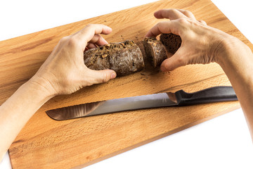 woman cutting a small loaf of whole wheat bread on a wooden board with a knife