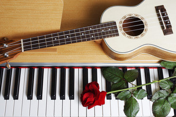 Ukulele and red rose on the piano keyboard.