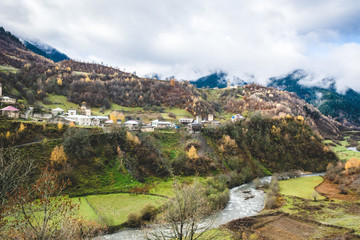 Panoramic view of small town placed on green hills of mountain valley in clouds, Svaneti 