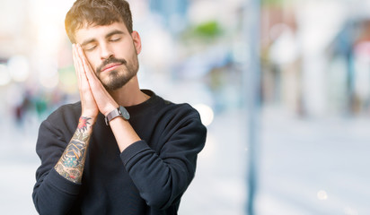 Young handsome man over isolated background sleeping tired dreaming and posing with hands together while smiling with closed eyes.