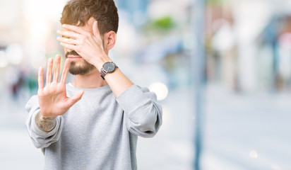 Young handsome man wearing sweatshirt over isolated background covering eyes with hands and doing stop gesture with sad and fear expression. Embarrassed and negative concept.