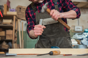 Carpenter working with a chisel and hammer in a wooden workshop. Profession, carpentry and manual woodwork concept.