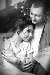 A loving couple in the arms of each other under the rug in the interiors of the room. Black and white images.