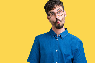 Fototapeta premium Young handsome man wearing glasses over isolated background making fish face with lips, crazy and comical gesture. Funny expression.