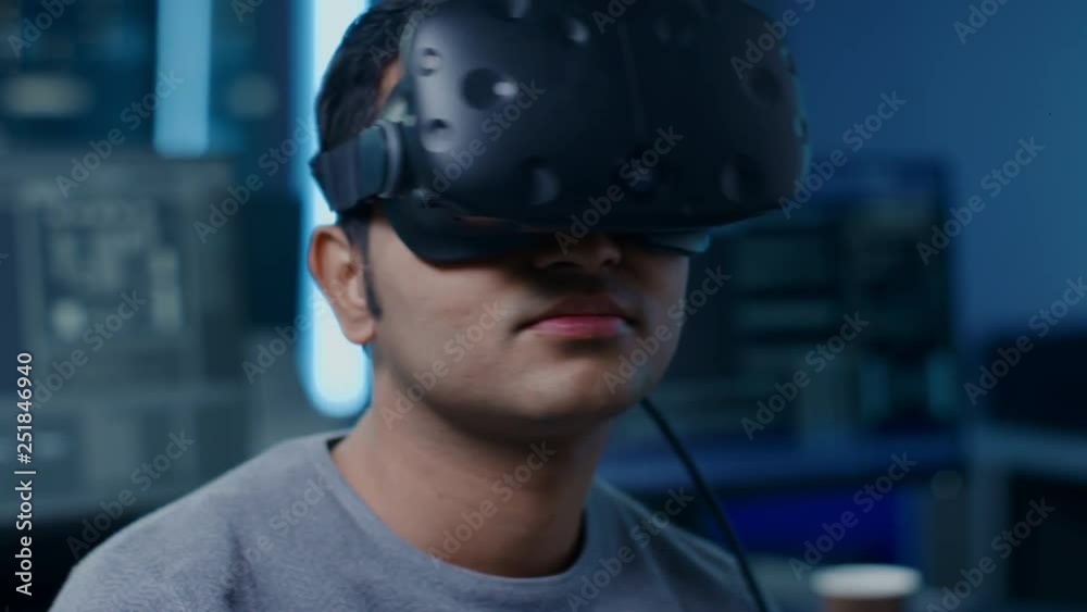 Aufkleber Portrait of Software Delevoper Puts On Virtual Reality Headset Holds Controllers and Starting Programming in VR. In the Background Technology Developing Studio with Computers and Monitors