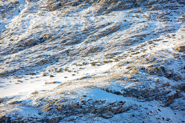 Snow-covered mountainside at sunset. You can see an abandoned building and two grazing deer.