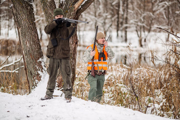 hunters armed with a rifle, standing in a snowy winter forest with duck prey