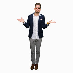 Young handsome elegant man wearing sunglasses and fashion blazer clueless and confused expression with arms and hands raised. Doubt concept.