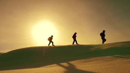 team of travelers follow each other along snow ridge against backdrop of yellow sunset. coordinated...