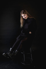 Fototapeta na wymiar portrait of a young girl in a black dress on a dark background sitting in the studio
