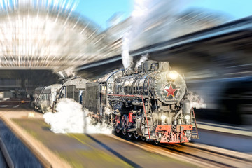Old steam train locomotive driving past the passenger platform of the station