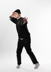 Naklejka premium Young freestyle dancer dressed in black jeans, sweatshirt, hat and gray sneakers is dancing in the studio on the white background