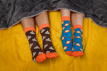 tw pairs of feet in funny colorful socks lying on the yellow bed with grey cover