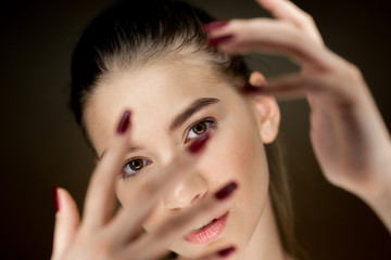 Fototapeta premium Portrait of young beautiful brown-haired girl with natural makeup holding her fingers in front of her face