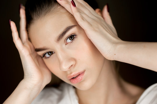 Portrait of young beautiful brown-eyes girl with natural makeup holding her hands on her head