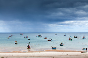 Fototapeta na wymiar scenic seascape fisherman life, a lot of traditional fishing wooden boat in the sea, storm is coming backgrounds, sand beach foreground. Rainy season. Chumphon, Thailand. Copy space.
