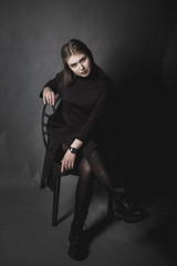 portrait of a young girl in a black dress on a gray background sitting in the studio