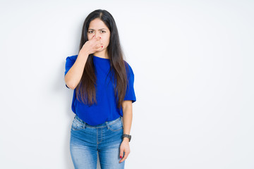 Beautiful brunette woman over isolated background smelling something stinky and disgusting, intolerable smell, holding breath with fingers on nose. Bad smells concept.