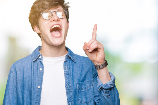 Young handsome man wearing glasses over isolated background pointing finger up with successful idea. Exited and happy. Number one.