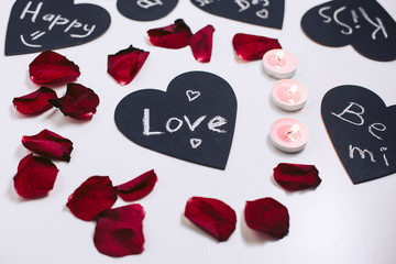 Black valentines with love text and petals of red roses on the background. Light decorative candles