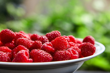 Red raspberries in a white bowl on blurred background
